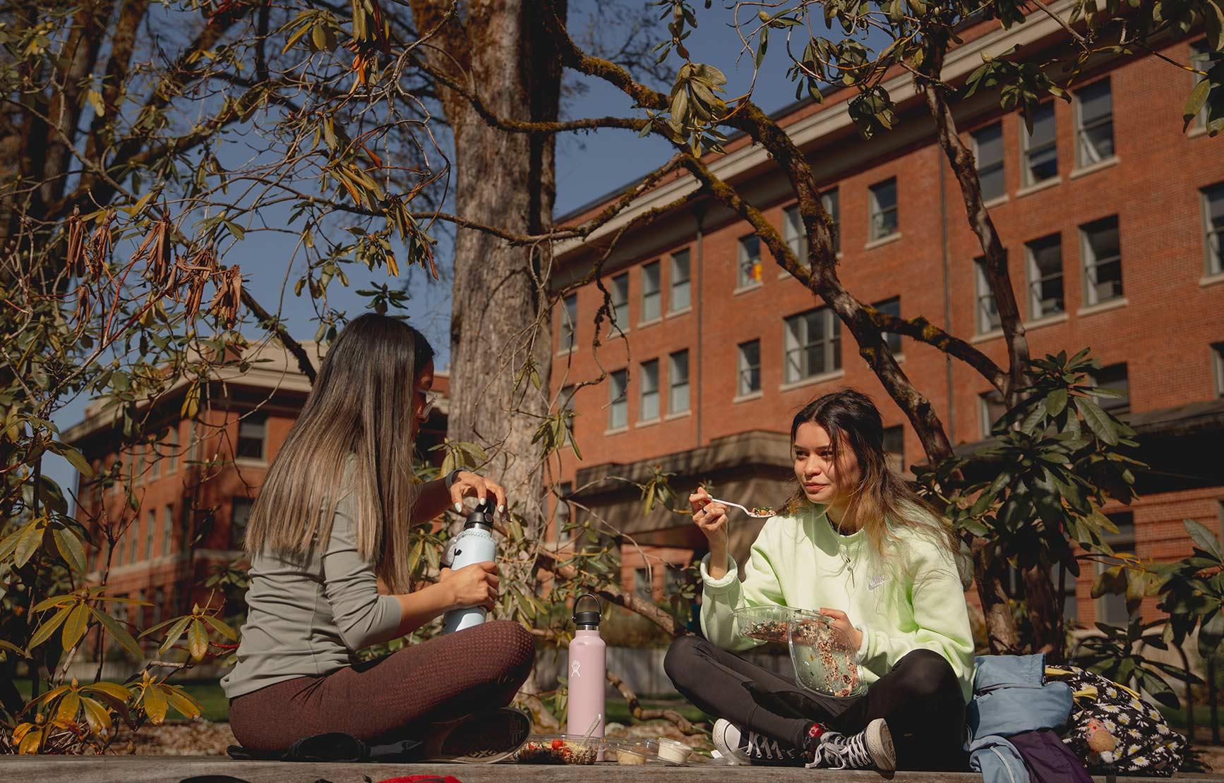 Two students sitting on a bench eating lunch outside of Strand Agriculture Hall.