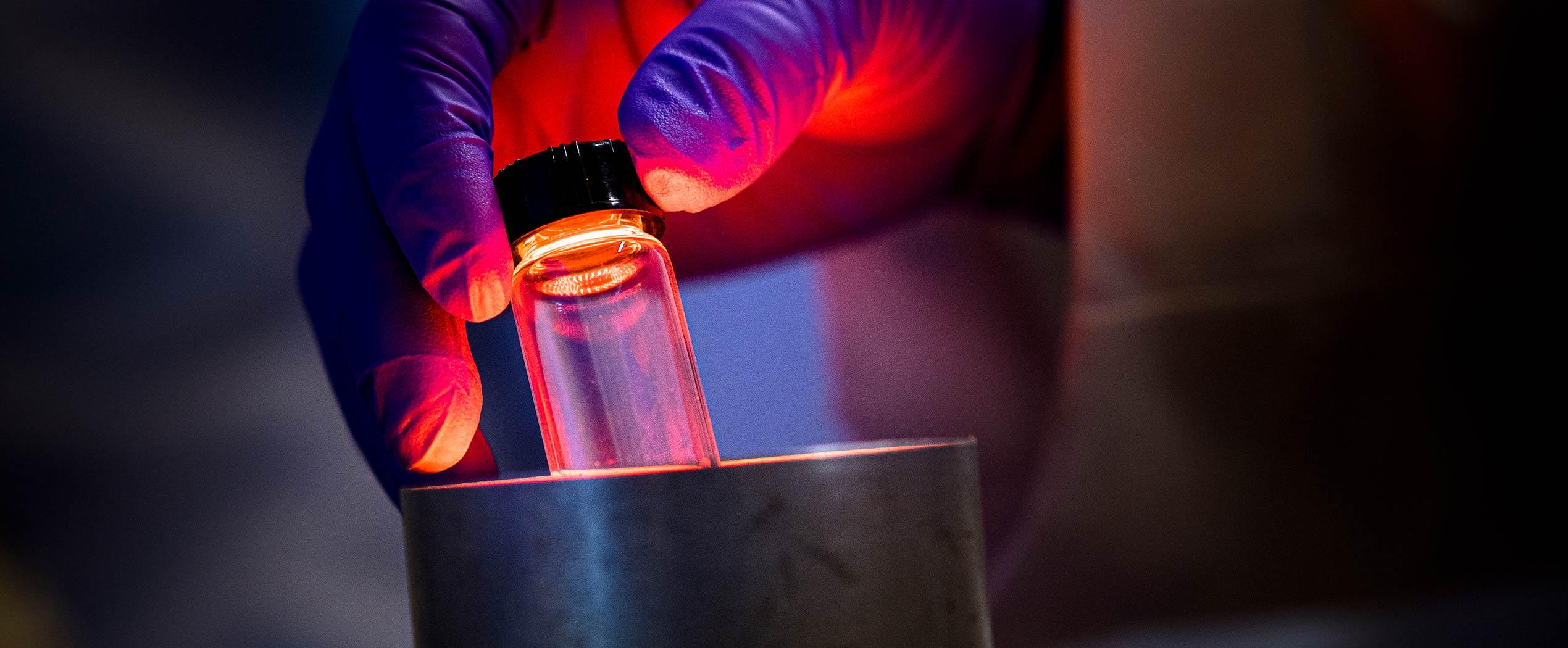A gloved hand putting a vial in a metal tube with a fluorescent red glow.