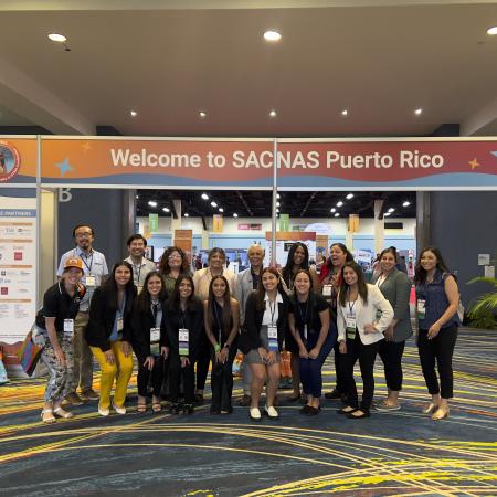 A group of individuals stands in front of an orange SACNAS Puerto Rico banner.